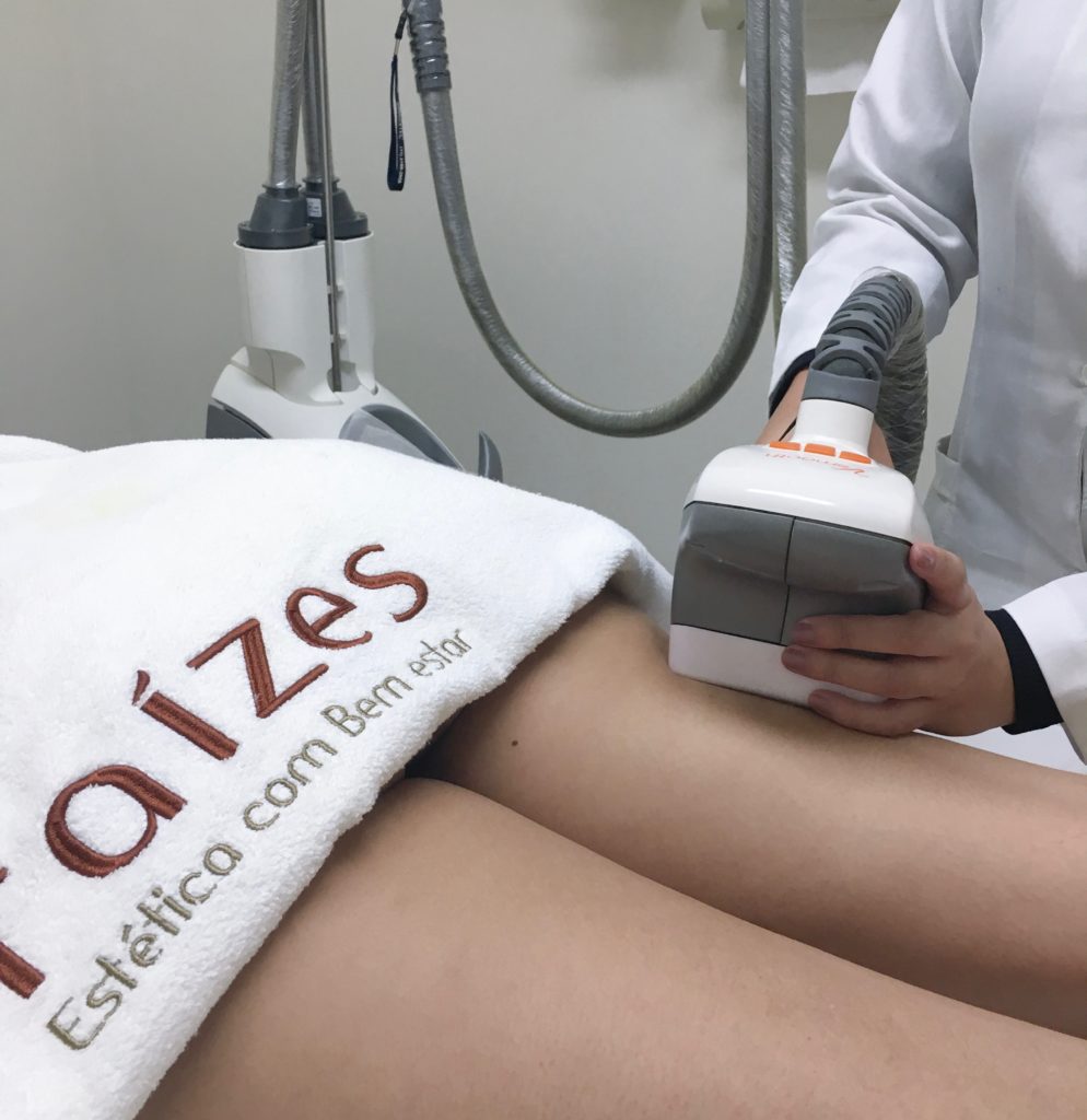 Mulher deitada de barriga para baixo, com o equipamento velashape na parte posterior de coxas.